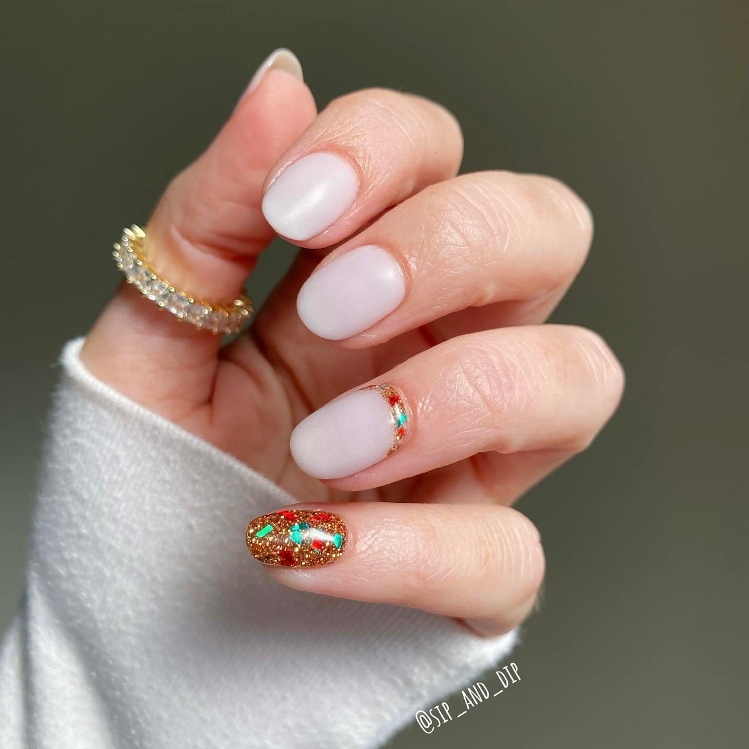 Short beige nude dip powder manicure with gold glitter and colorful foil accent nail on ring finger.