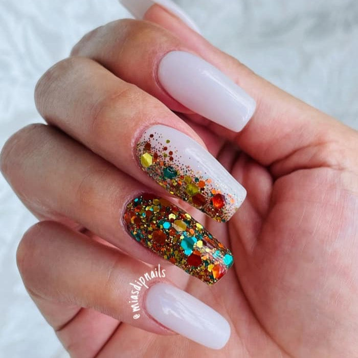 Glossy pale nude dip powder manicure with multicolored glitter accent nail on ring finger.