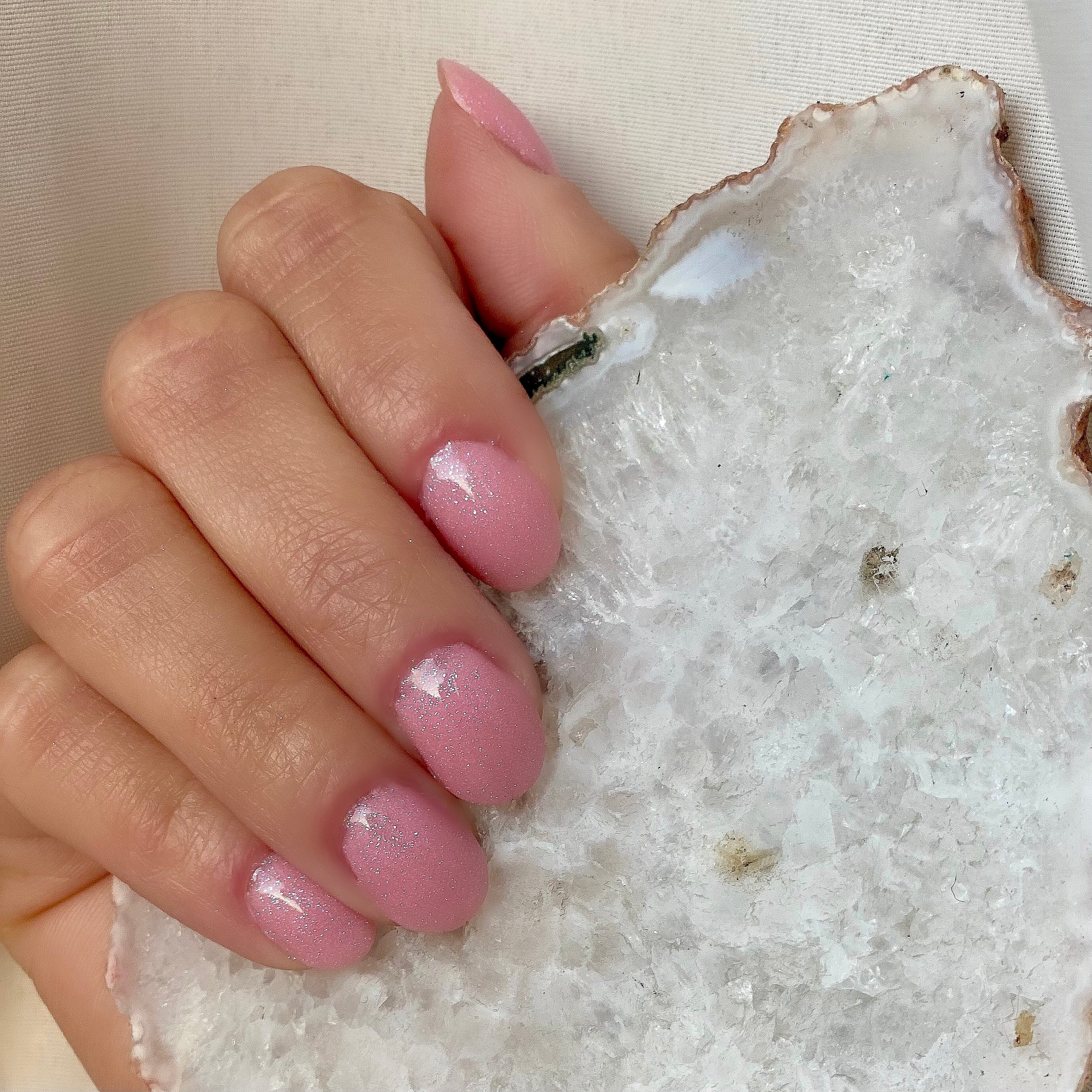 Short almond-shaped nails with glossy pink-purple glow-in-the-dark dip powder polish holding a white geode stone.