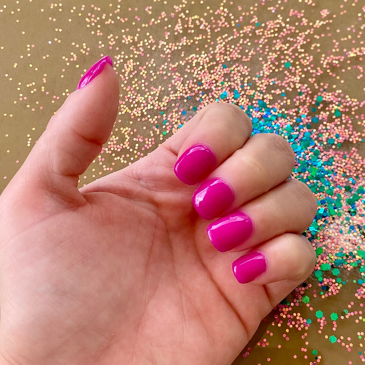 Bright neon pink glossy dip powder nails on hand with colorful glitter background.