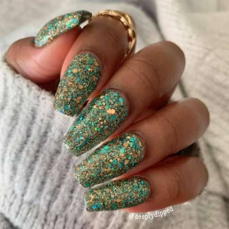 Long nails with chunky blue and gold glitter dip powder on a hand wearing a gray knit sweater.