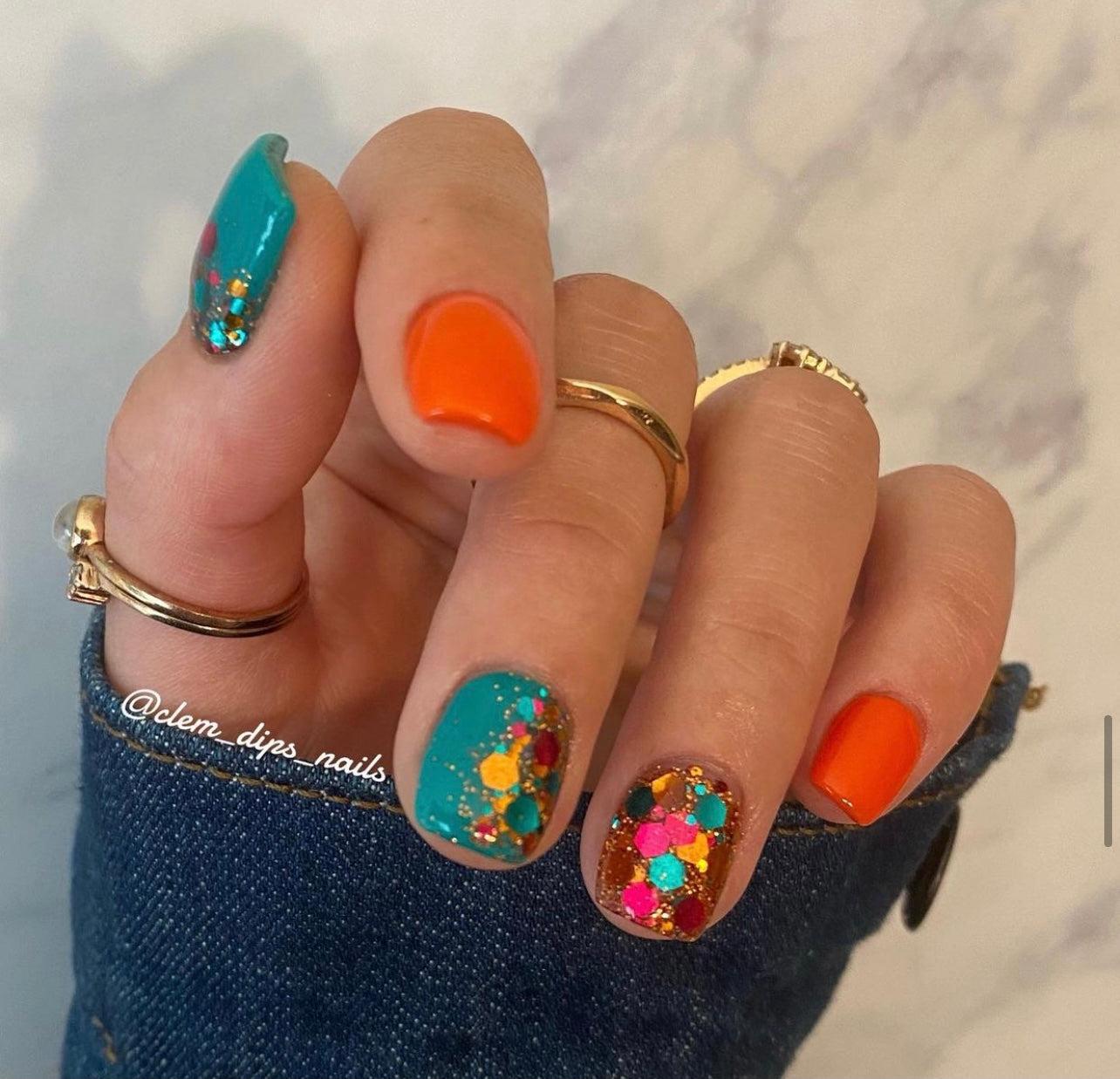 Bright orange solid dip powder on index and pinky nails, teal base with colorful floral accents on middle and ring nails.