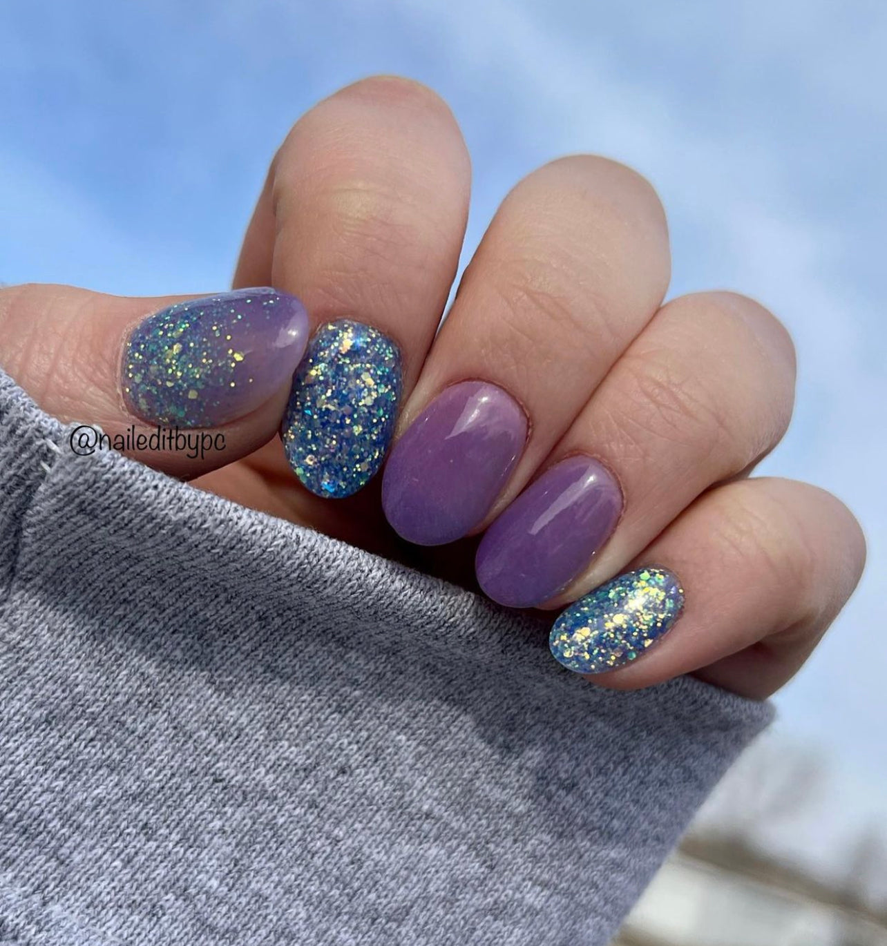 Short acrylic nails painted with purple and blue chunky holographic glitter dip powder polish.