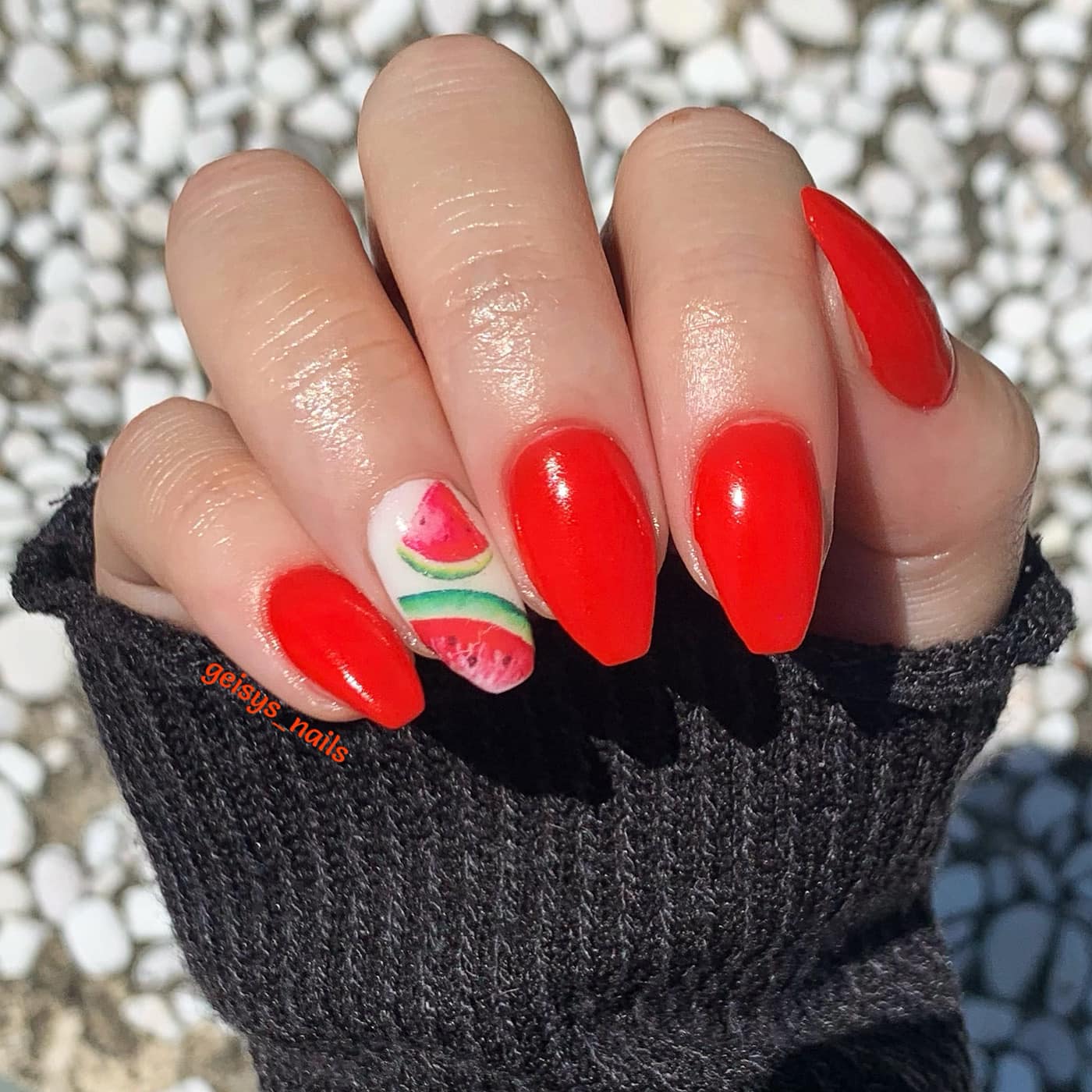 Bright red almond-shaped nails with one accent nail featuring hand-painted watermelon slices and black seeds.