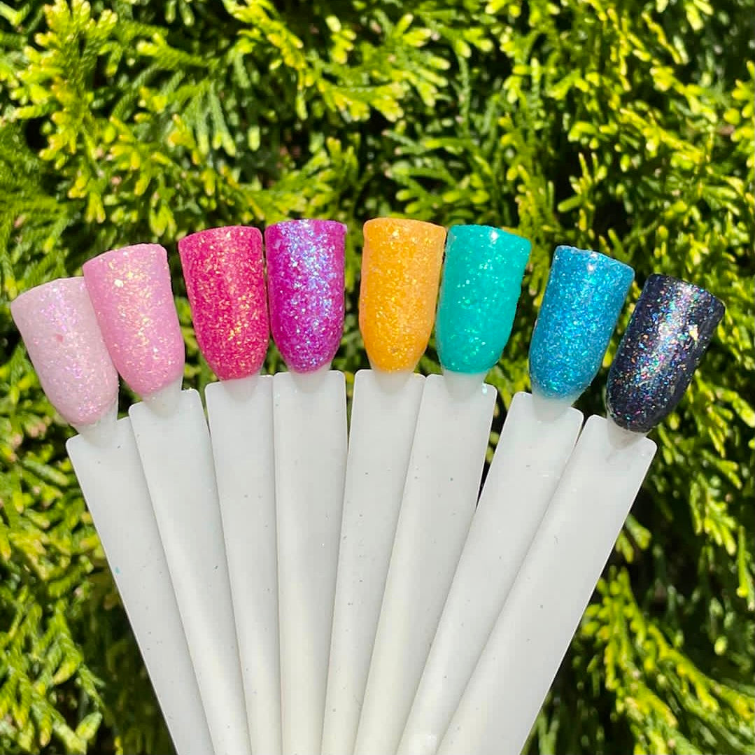 Multicolor glitter dip powder nail swatches in pink, purple, yellow, teal, blue, and dark purple shades against green.