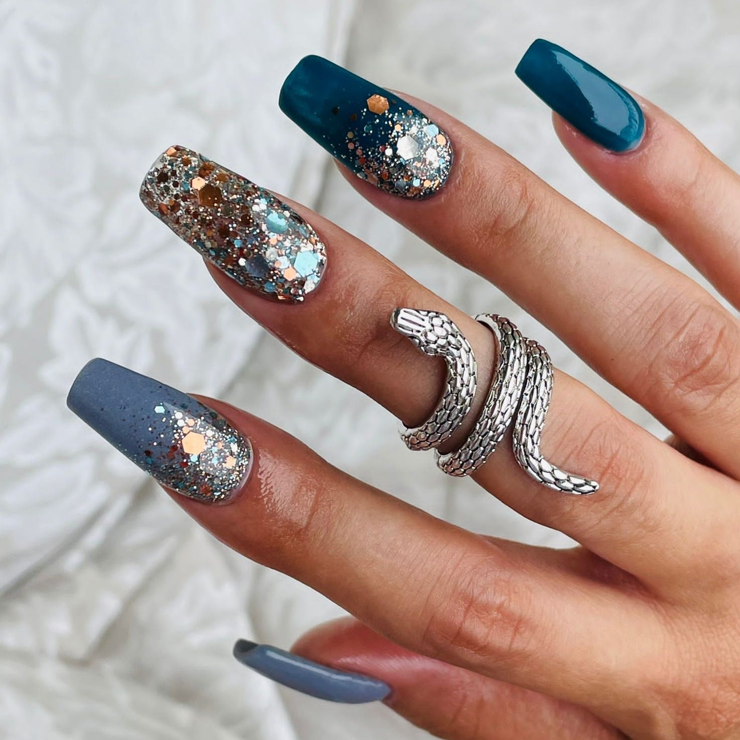 Long coffin nails with glossy blue polish and chunky silver, copper, and multicolor glitter accent nails on middle and ring.
