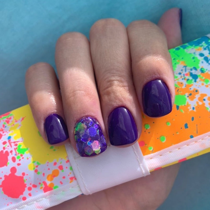Purple glossy dip powder nails with a glitter accent nail featuring blue and purple hexagonal flakes.