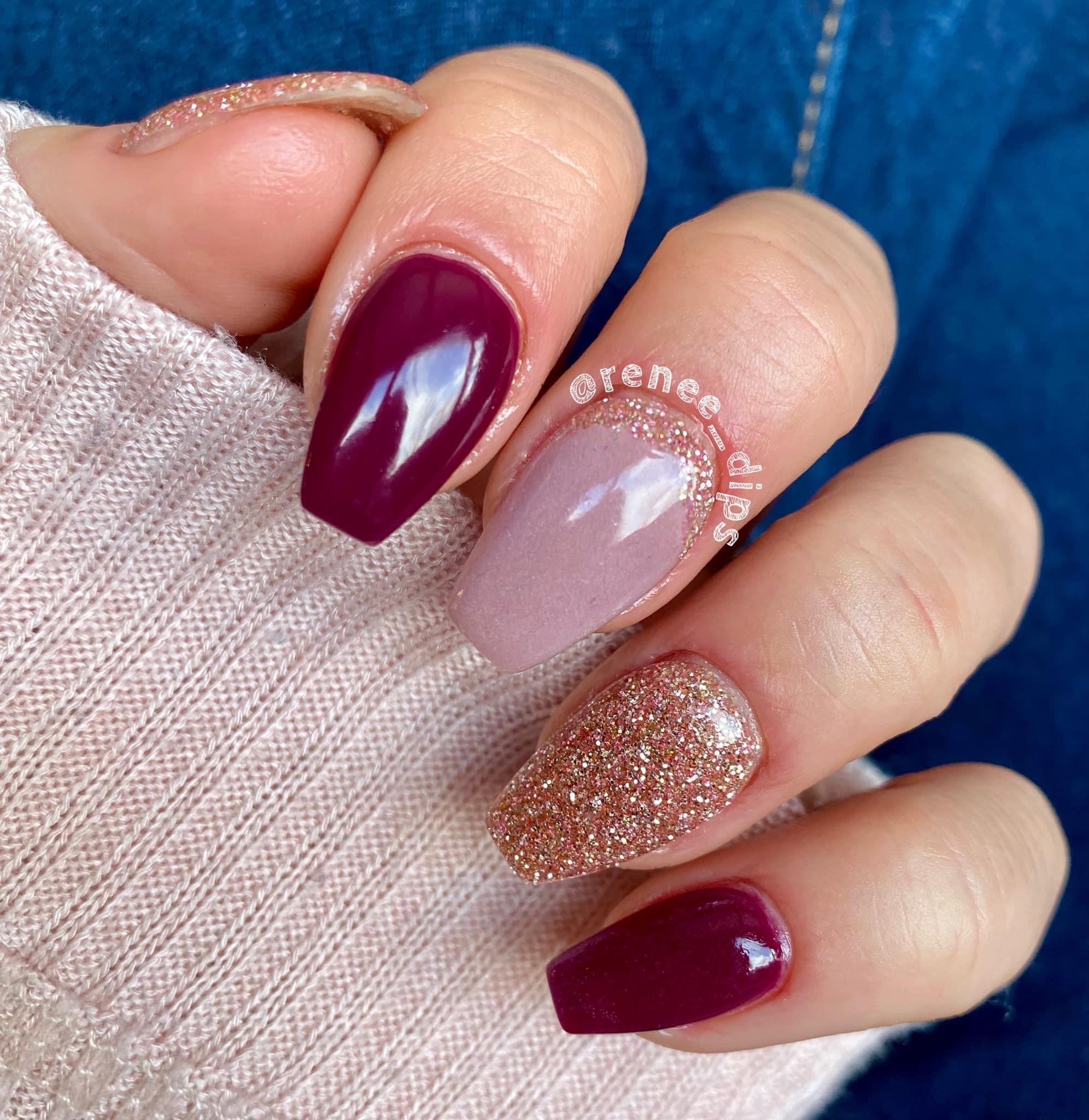 Manicure with glossy deep wine purple and nude dip powder nails, one glittery rose gold accent nail.