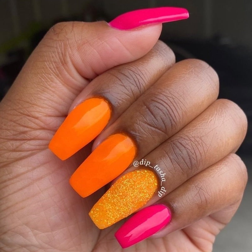Bright neon orange dip powder nails with one glitter textured nail and two hot pink nails on a medium brown hand.