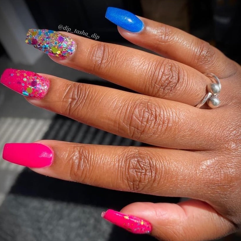 Hand with long acrylic nails in bright pink, blue, and glittery multicolor designs on natural skin tone.