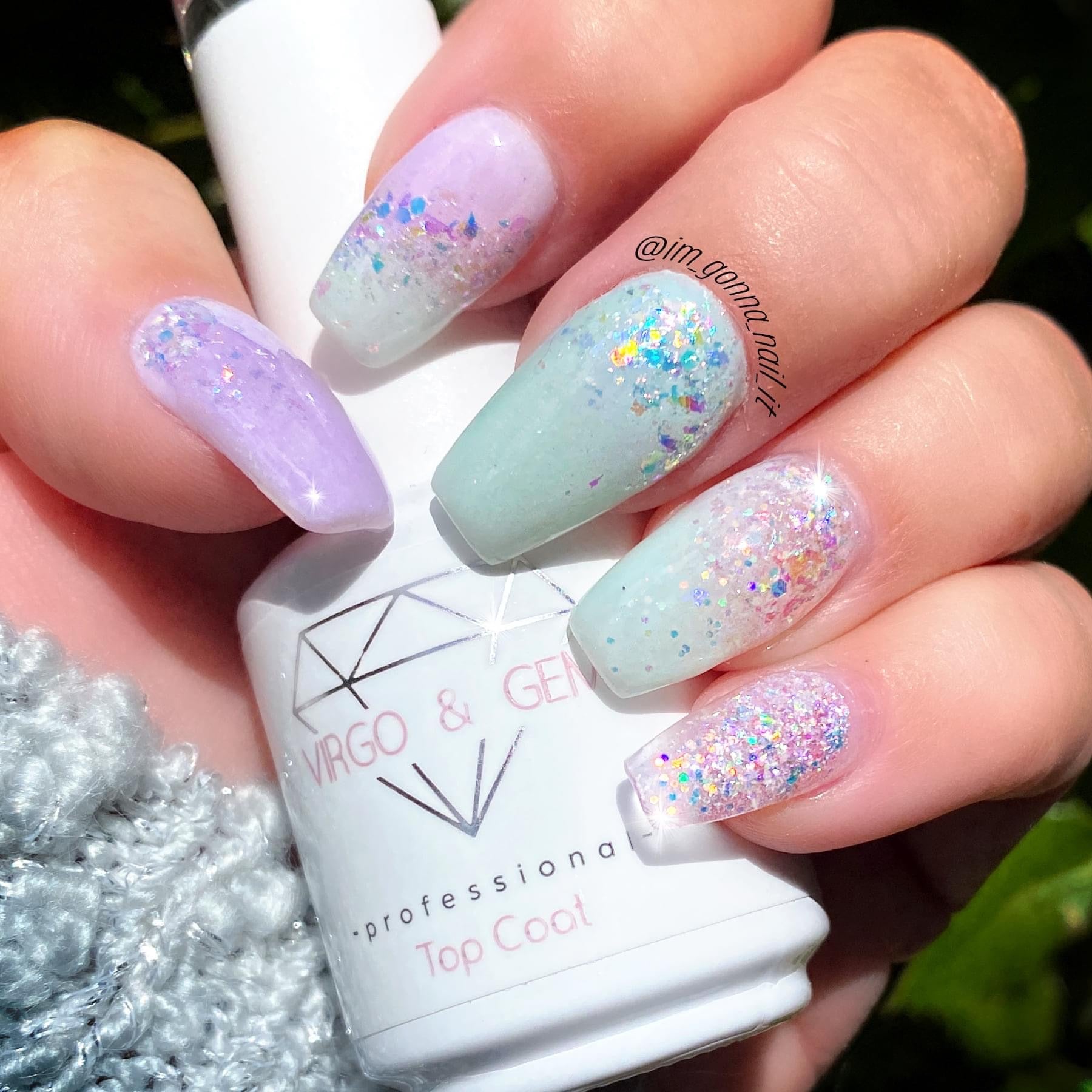 Hand with light blue and pastel purple dip powder nails featuring iridescent glitter over a white top coat bottle labeled.