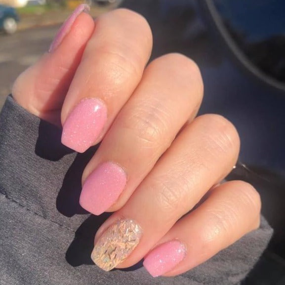 Hand with pink shimmer nails and one accent nail featuring intricate beige and brown cracked design.