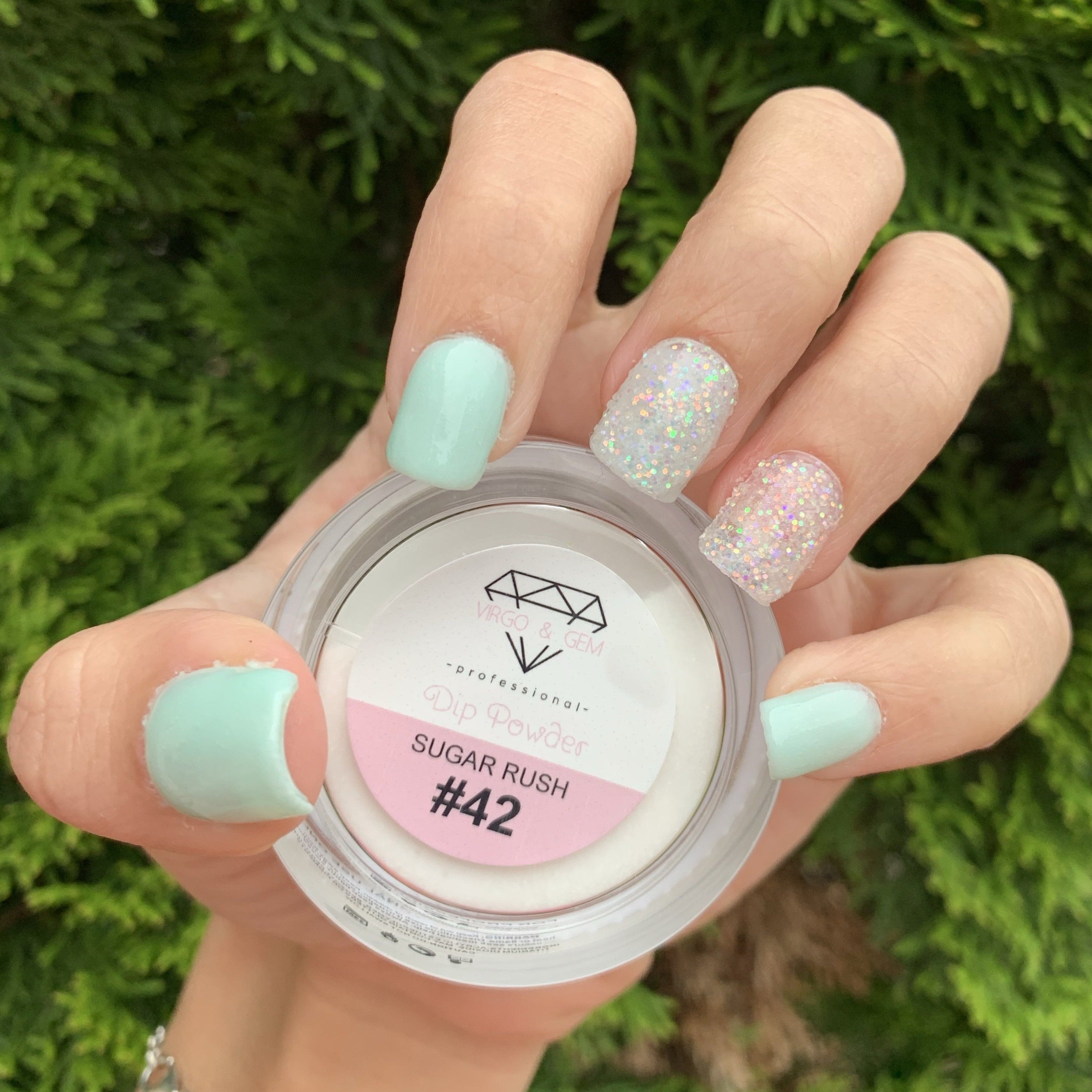Light blue solid dip powder on nails with two nails featuring iridescent glitter over clear base, holding open jar labeled.
