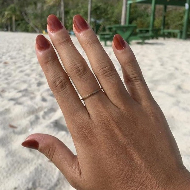 Hand with medium brown solid nail polish on short nails, wearing thin silver rings.