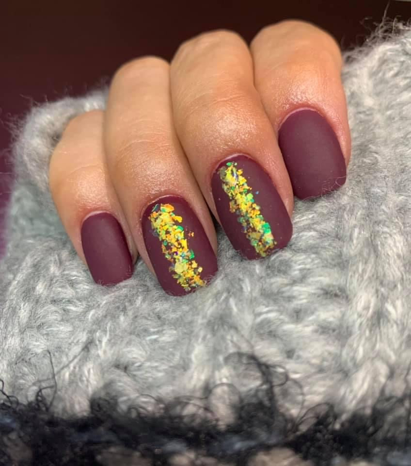 Matte wine purple nails with gold foil accent on middle and ring fingers over a cozy gray sweater background.
