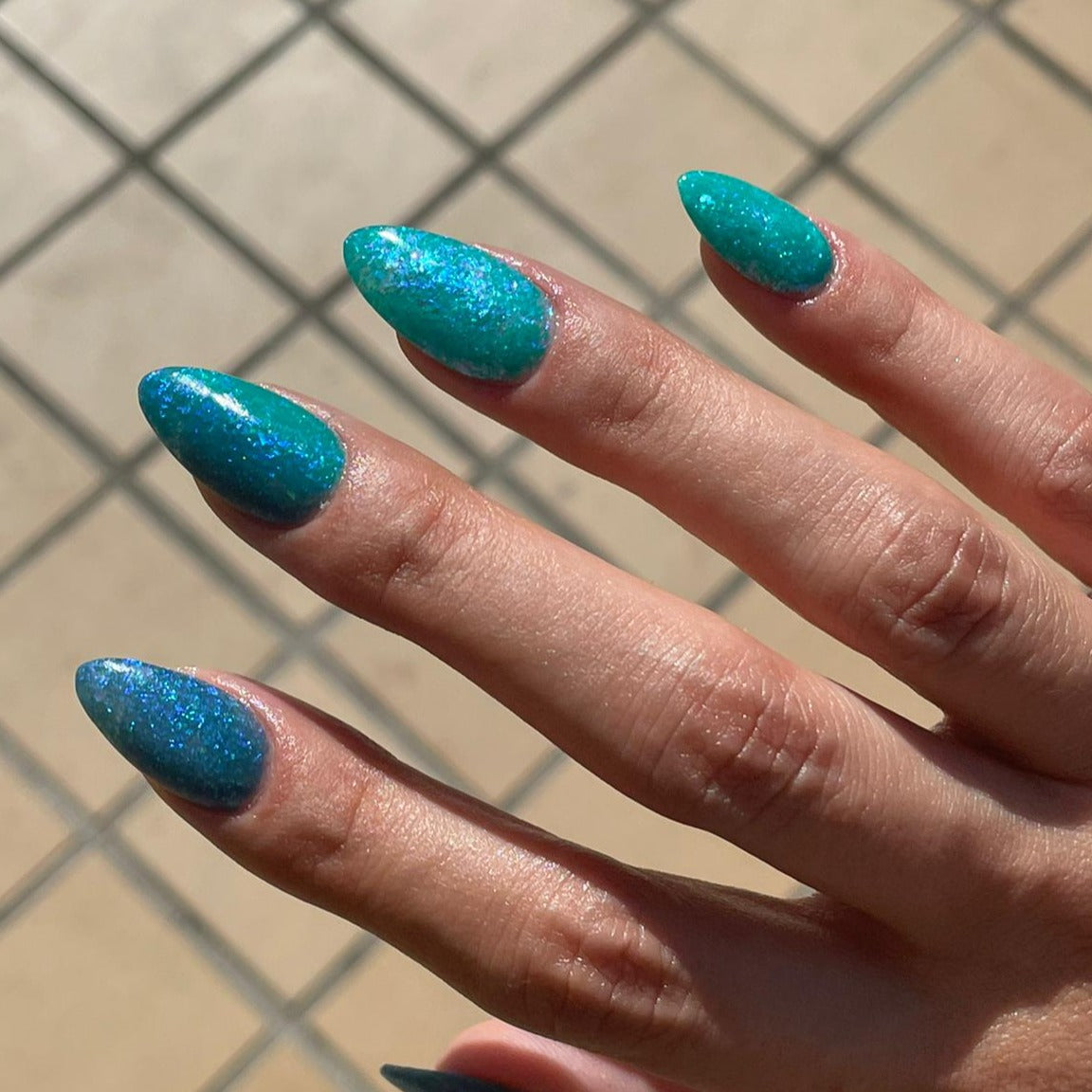 Teal and blue almond-shaped nails with multicolor chameleon flake glitter sparkle under sunlight.
