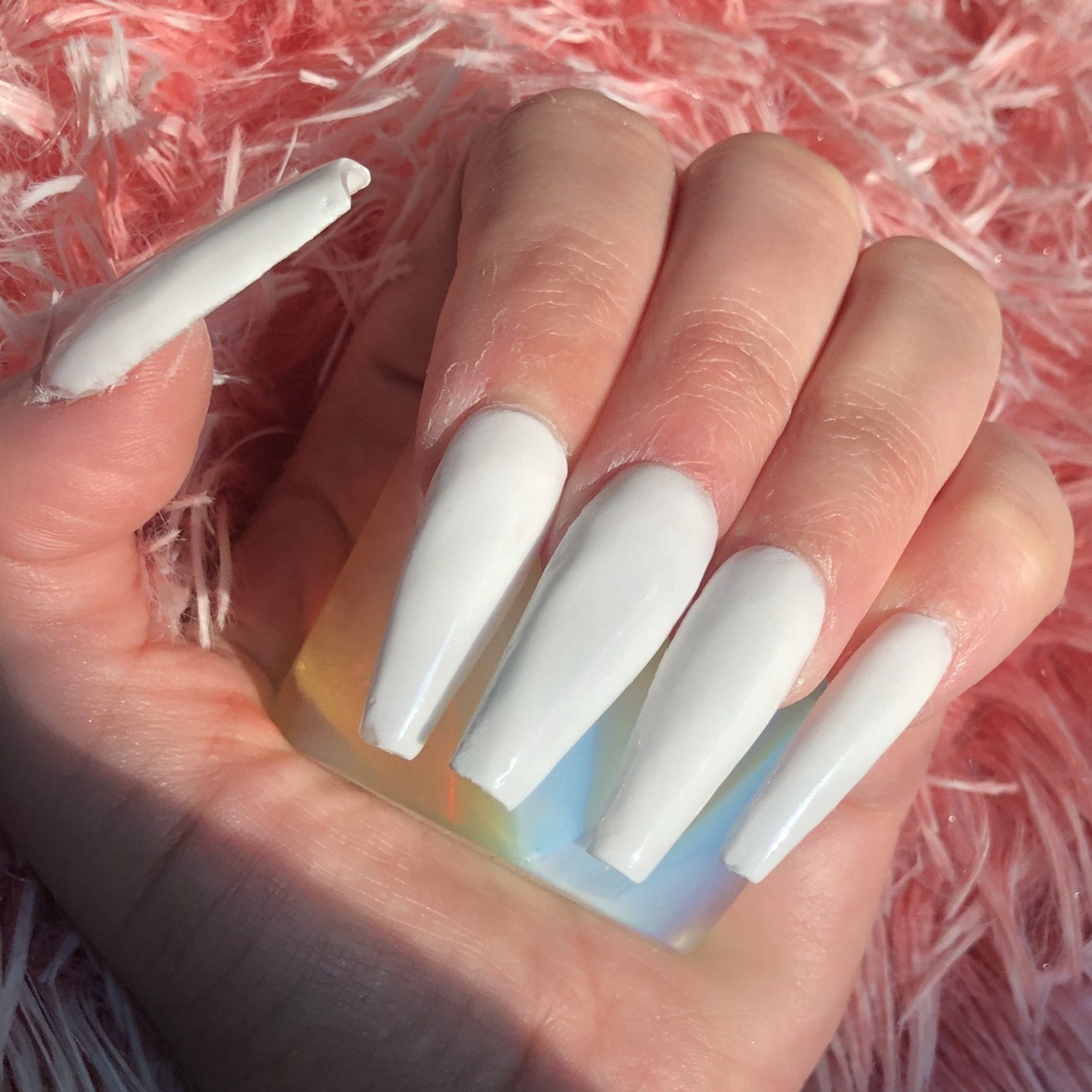 Long coffin-shaped nails with glossy solid white polish against a textured pink background.