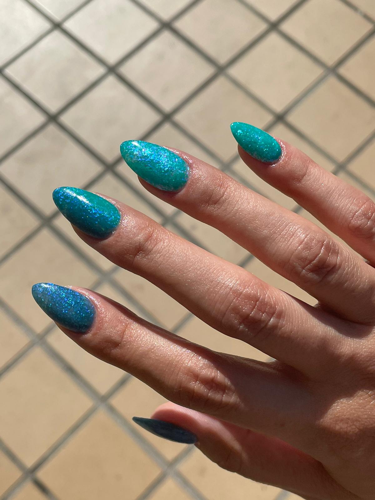 Teal blue glitter dip powder with multicolor chameleon flakes on long almond-shaped nails.
