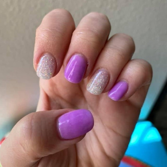 Manicure with alternating iridescent white glitter and vibrant purple glossy nails on short square tips.
