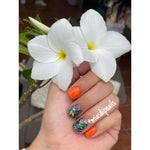 Hand with bright orange and multicolored glitter dip powder nails holding two white plumeria flowers.