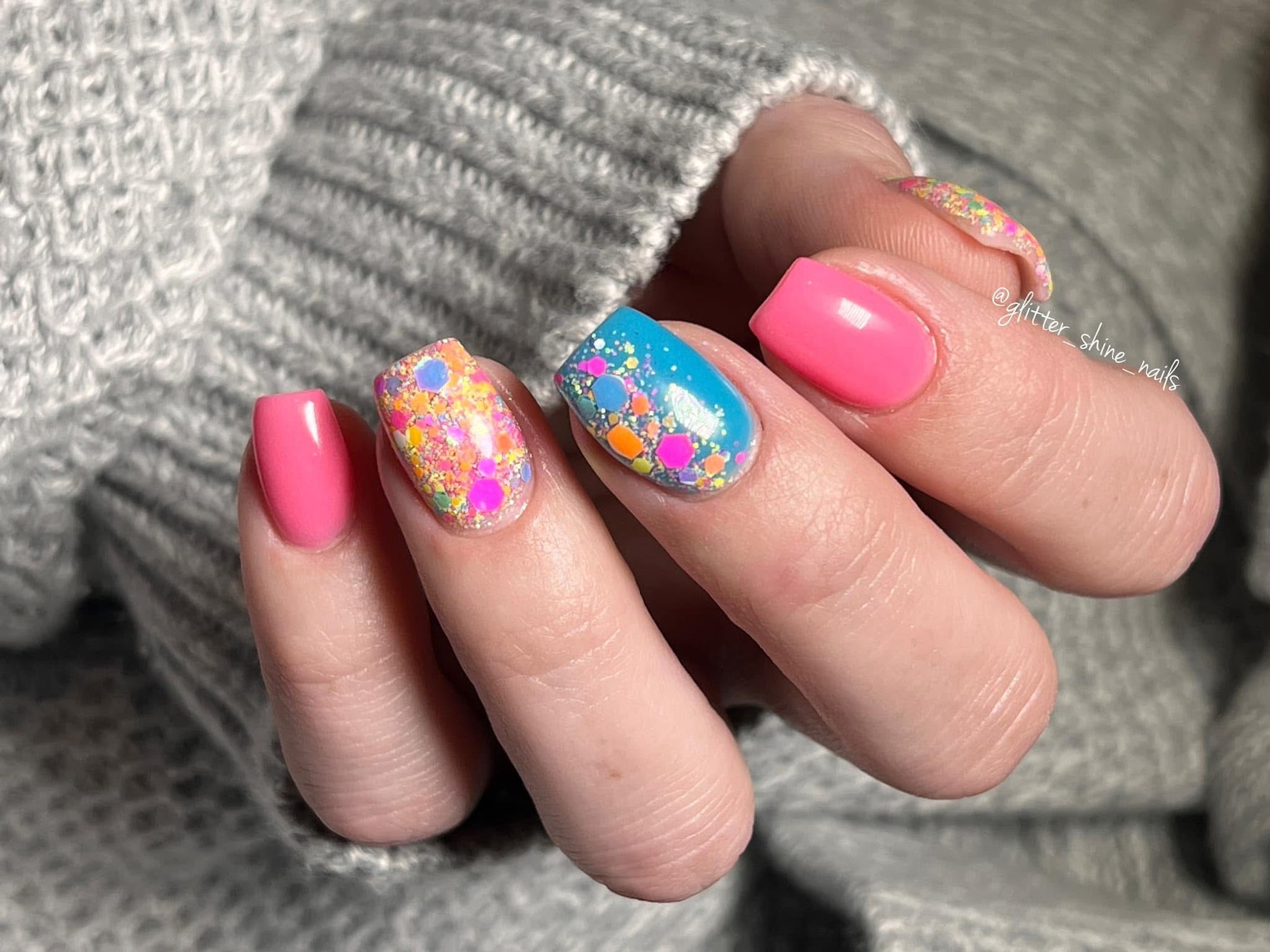 Hand with pink solid nails and two accent nails featuring colorful floral and glitter dip powder designs.