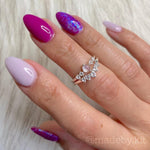Manicured hand with almond-shaped nails in shades of pale pink, magenta, and iridescent purple glitter polish.