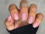 Light pink nails with fine shimmer polish on a hand wearing a silver ring and black sleeve.