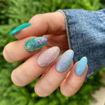 Hand with long almond nails in solid light blue, holographic glitter, and blue-pink iridescent dip powder designs against.