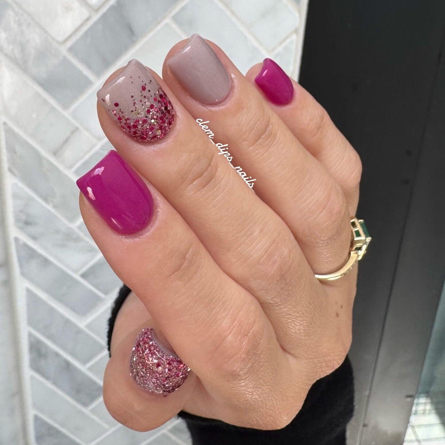 Hand with pink and glittery nails dip powder against a tiled wall background