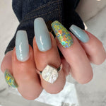 Long square nails with pastel blue polish and one accent nail featuring multicolor chunky glitter on a clear base.