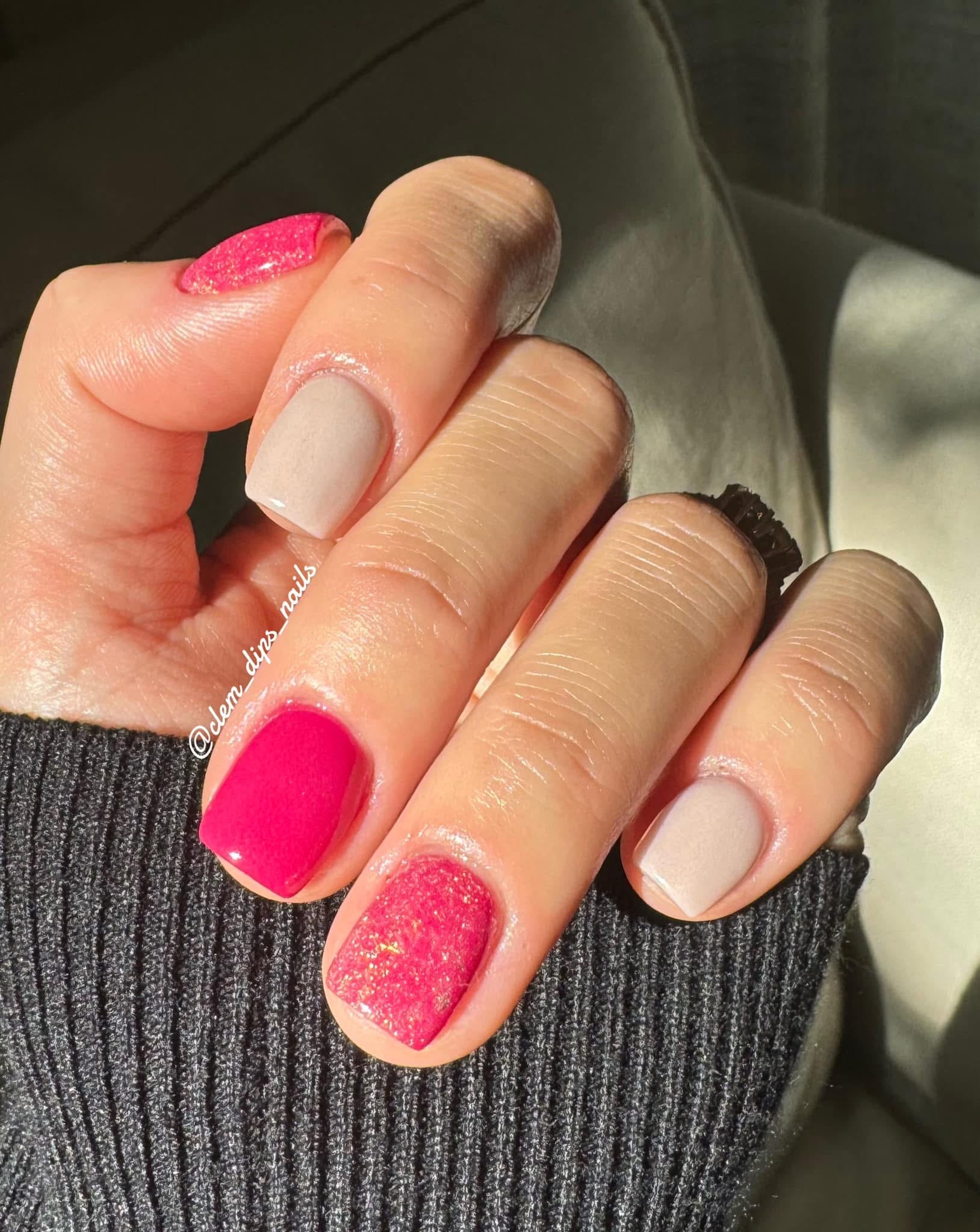 Hand with neutral beige and bright pink dip powder nails, pink nails glittered, natural light.