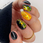 Glossy black nails with yellow and green floral glitter accents on almond-shaped tips.
