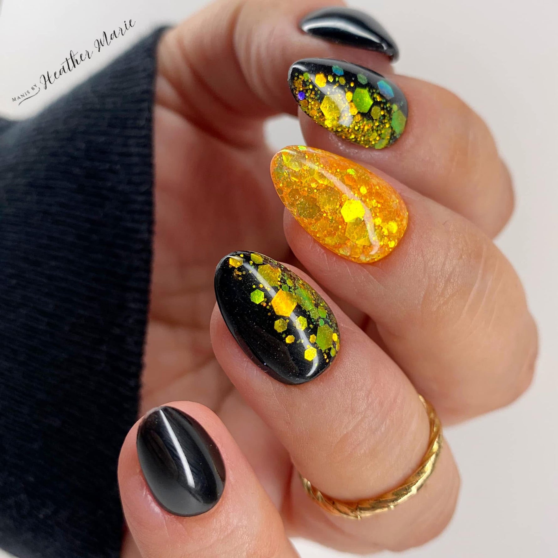 Glossy black nails with yellow and green floral glitter accents on almond-shaped tips.