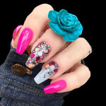 Hand with long nails painted bright pink, chunky multicolor glitter on accent nails, wearing turquoise rose ring and denim.