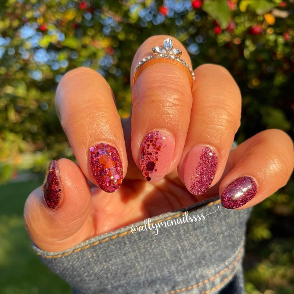 Burgundy and purple glitter dip powder nails with fine and chunky glitter on short almond-shaped nails.