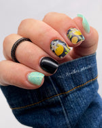 Black dip powder nails with glossy finish, featuring accent nails with pastel floral design on matte black base.