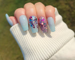 Light blue matte nails with two accent nails featuring pink, purple, and silver glitter on a short square shape.