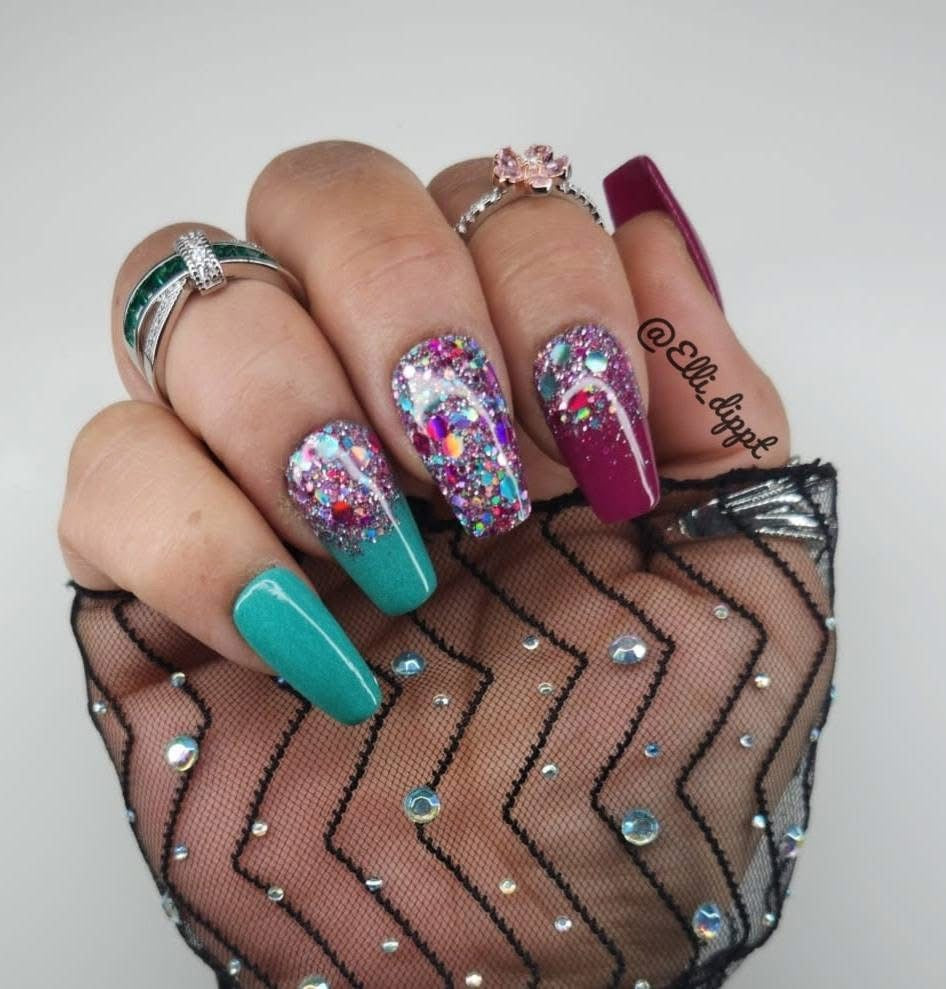 Long nails with teal, deep pink, and chunky multicolor holographic glitter polish on chevron mesh fabric background.