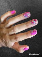 Pink nails with chunky blue, orange, and multicolor glitter on ring and middle fingers.