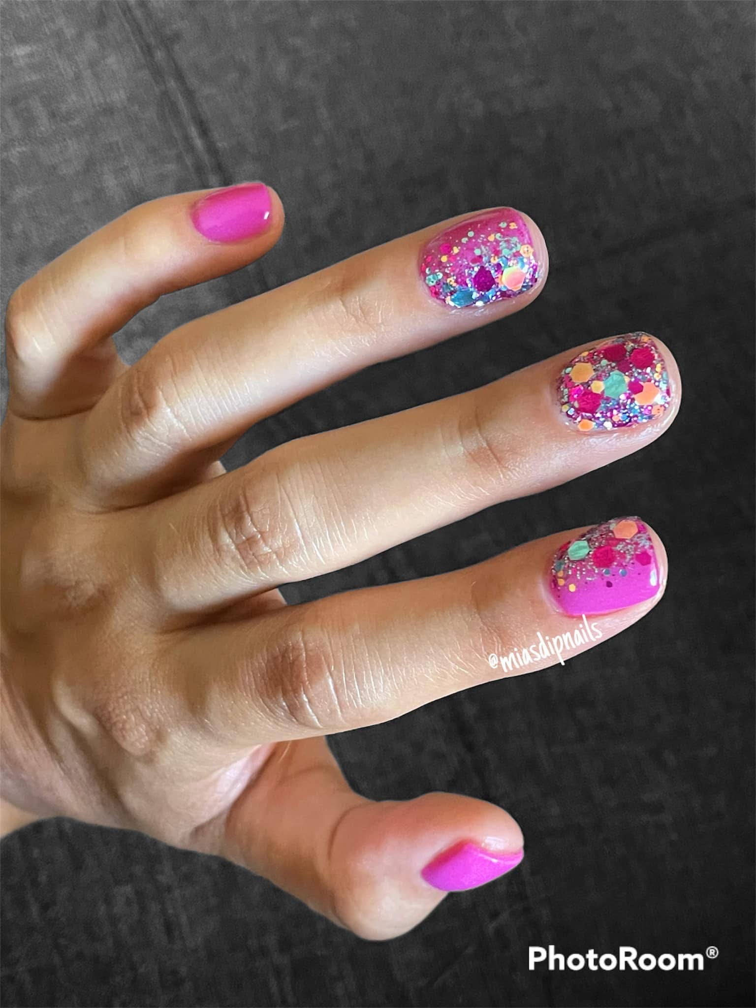 Pink nails with chunky blue, orange, and multicolor glitter on ring and middle fingers.