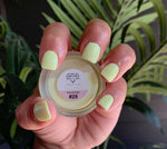 Hand with short pistachio green matte nails holding a small jar of dip powder labeled 