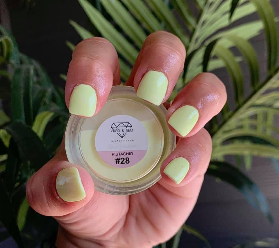 Hand with short pistachio green matte nails holding a small jar of dip powder labeled #28 Pistachio.