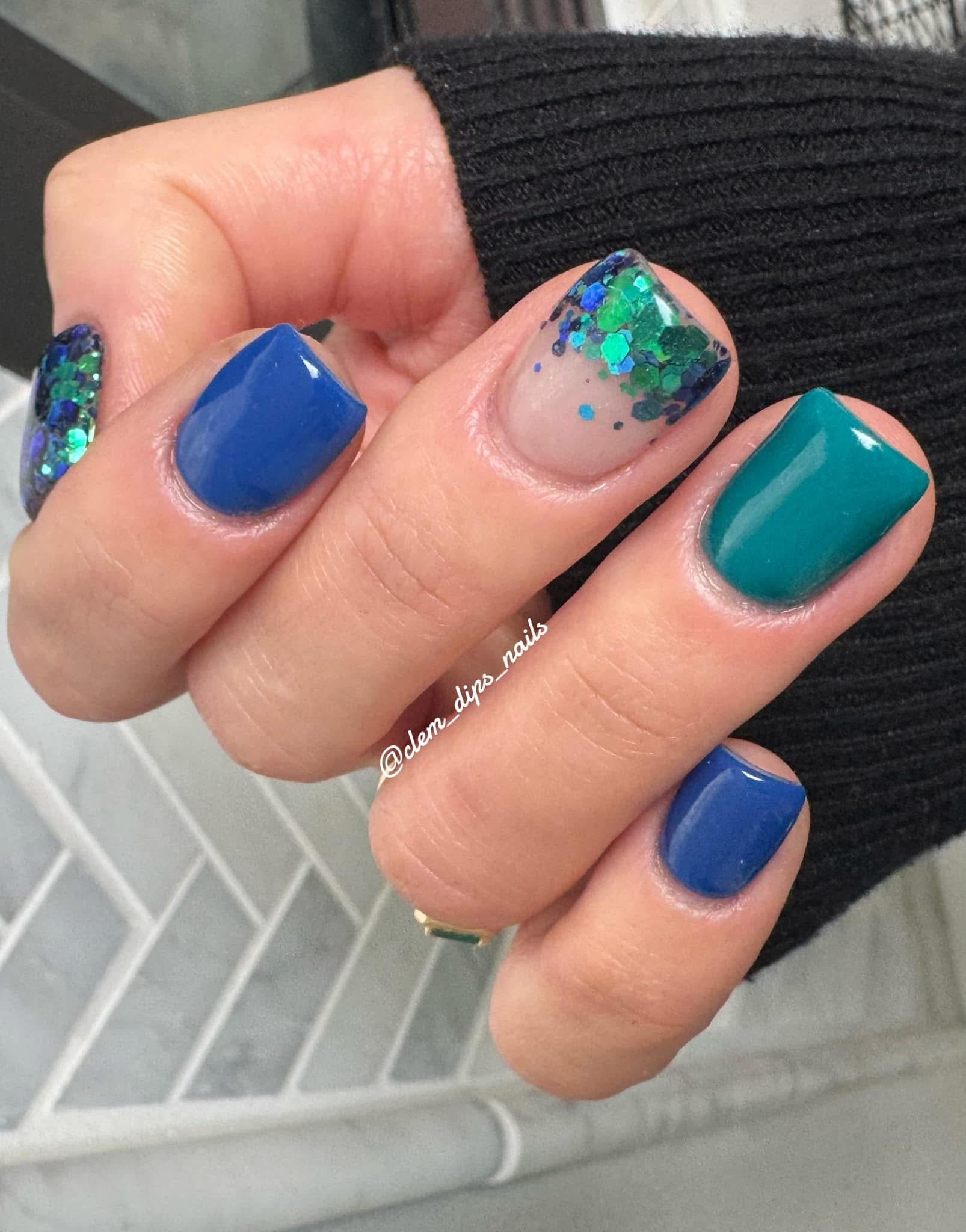 Nails with chunky blue, green, and teal glitter dip powder and solid blue and teal polish accents.