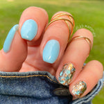 Light blue dip powder nails with gold and turquoise mosaic accent nails and delicate gold rings.