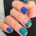 Glossy deep blue and teal solid nail polish with clear nail art featuring green and blue glitter accents.
