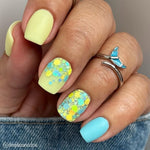 Matte pistachio green nails with yellow and blue hex glitter accent nails and silver butterfly ring on finger.
