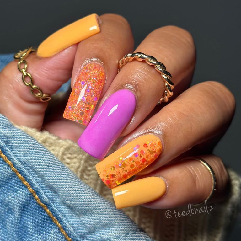 Hand with vibrant nails featuring DP341 Lilac Haze glitter dip powder, orange, and pink shades, showcasing a creative nail design.
