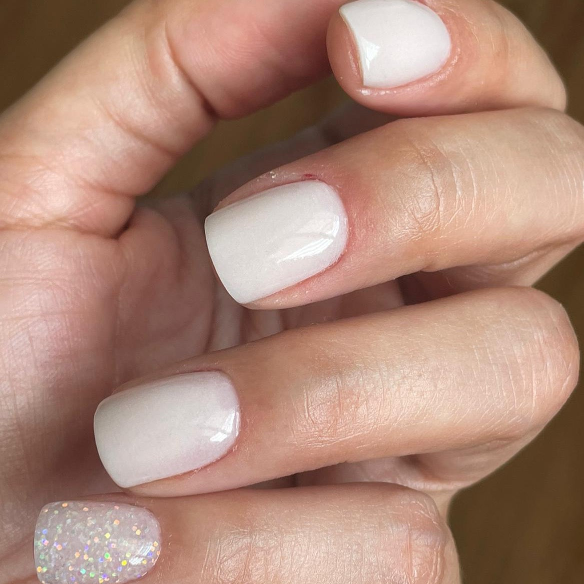 Short natural white gel nails with one accent nail featuring fine iridescent glitter polish.