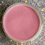 Bright solid pink dip powder in a clear round container on a sparkly holographic background.