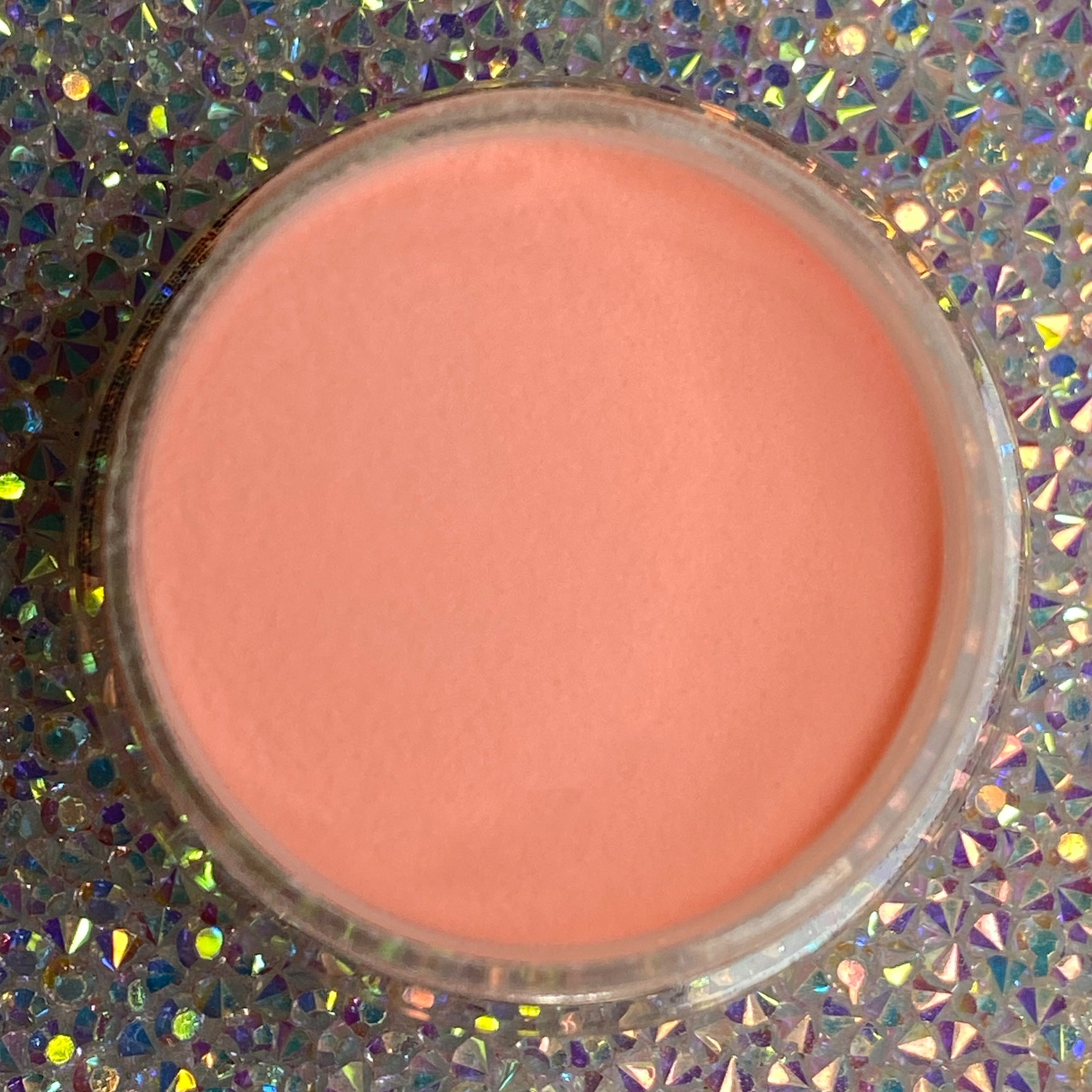 Open jar of smooth pastel coral-orange dip powder on holographic surface.